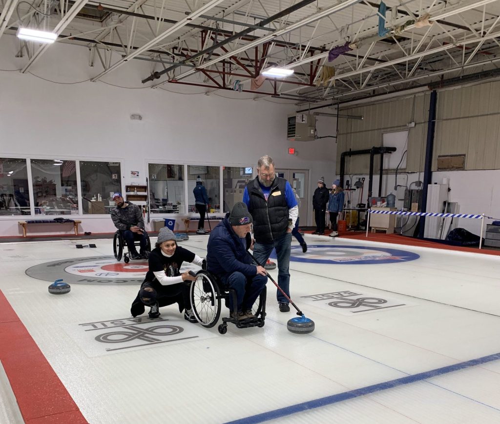 A wheelchair curler being assisted by his family as he prepares to throw the curling rock.