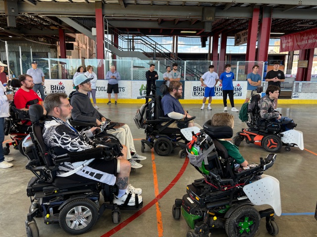 Power wheelchair users listen to coaches at the start of a power soccer clinic.