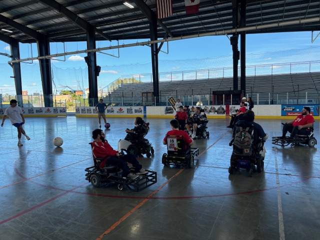 A group of athletes in power wheelchairs take part in a drill, avoiding getting hit by a soccer ball.