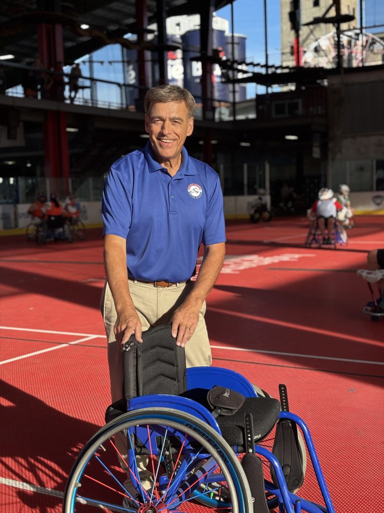 A solo shot of Norm Page behind a sports wheelchair and wearing a blue GBAS polo shirt.