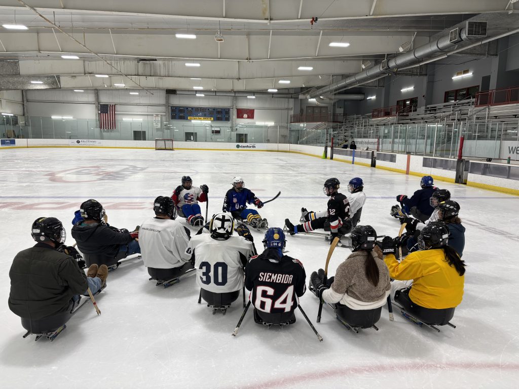 Group of sled hockey athletes listen to directions on the ice.
